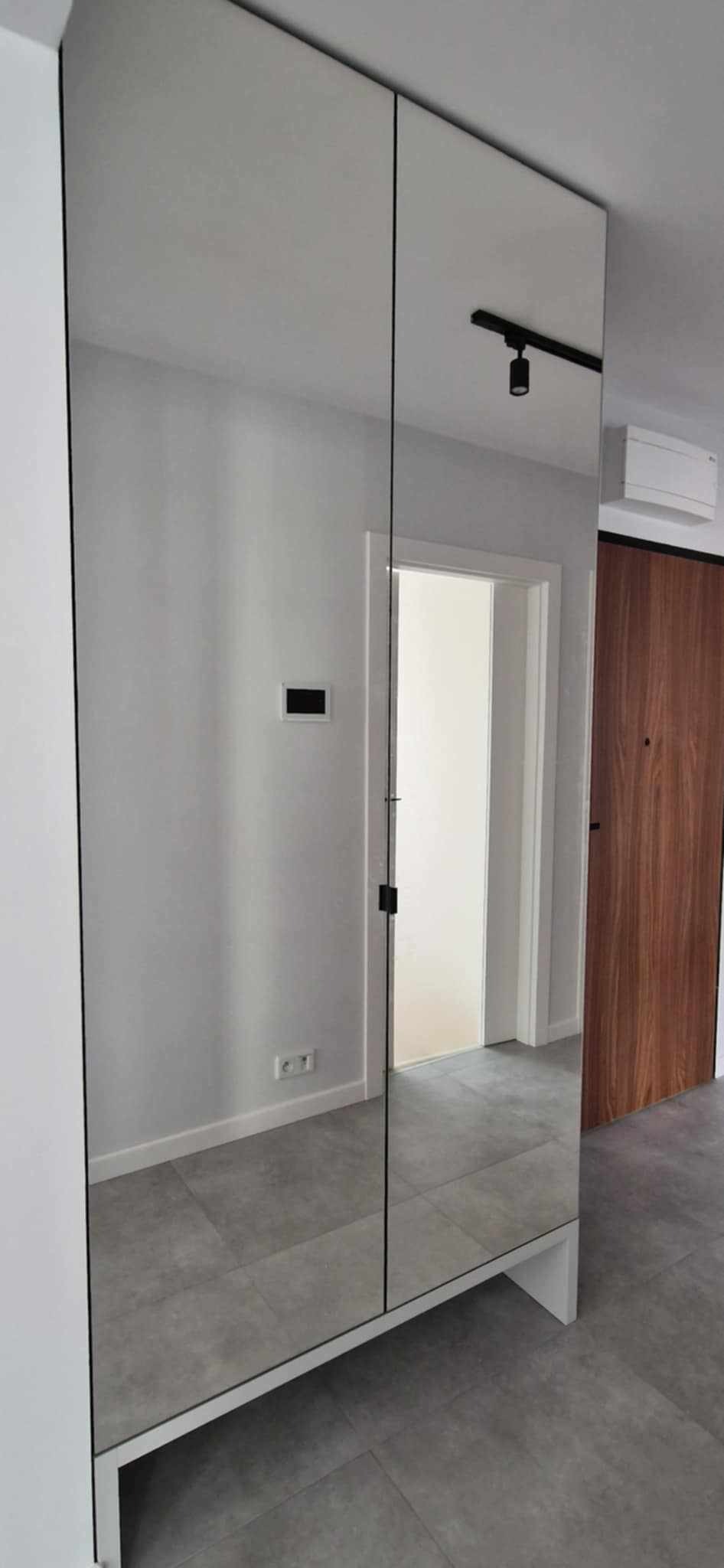 Nowoczesna szafa wnękowa z lustrzanymi drzwiami, czarne detale, szara podłoga, minimalistyczne wnętrze.