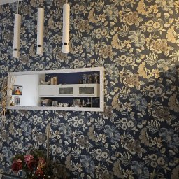 Stanisław Kościański - Ściana po remoncie z nową tapetą w kwiaty, oświetleniem i dekoracyjną ramą eksponującą zawartość szafek kuchennych.