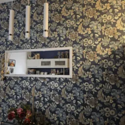 Ściana po remoncie z nową tapetą w kwiaty, oświetleniem i dekoracyjną ramą eksponującą zawartość szafek kuchennych.