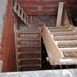 Viktoriia Nikolova Auto-LuX - Konstrukcja szalunku schodów w surowym stanie, widoczne zbrojenie i czerwona cegła w tle.