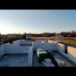 Viktoriia Nikolova Auto-LuX - Wznoszone ściany parteru z bloczków betonu komórkowego na fundamencie, widoczne zapasy materiału budowlanego na placu budowy domu jednorodzinnego w słoneczny dzień.