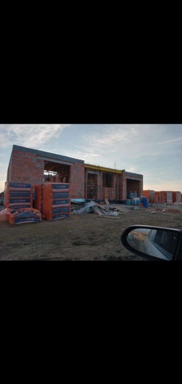 Budowa domu murowanego z bloczków ceramicznych Porotherm, widok zza szyby samochodu, palety bloczków na pierwszym planie.