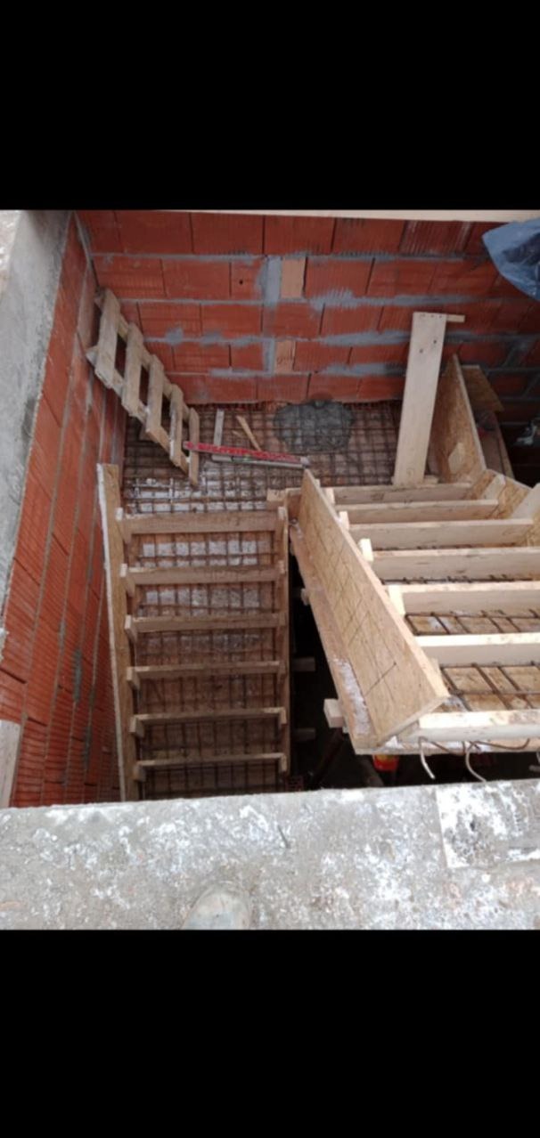 Konstrukcja szalunku schodów w surowym stanie, widoczne zbrojenie i czerwona cegła w tle.