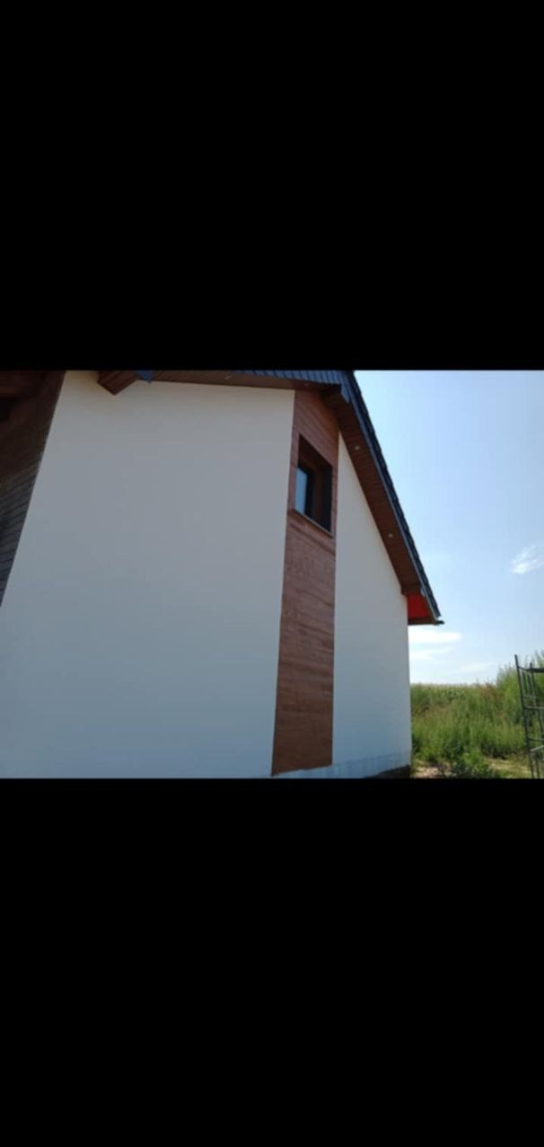 Ściana domu murowanego z oknem, fragment elewacji z drewnianą okładziną, widok z zewnątrz w słoneczny dzień.