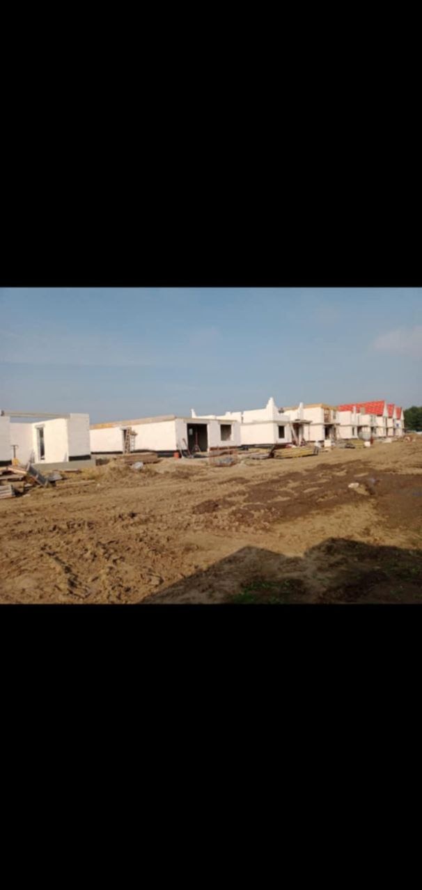 Wznoszenie zespołu budynków jednorodzinnych w stanie surowym otwartym, widoczne ściany z pustaków i elementy więźby dachowej, teren budowy w trakcie prac ziemnych.