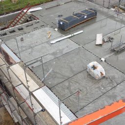 Roof Craft VASYL ANDROSHULIK - Widok z góry na mokry dach w trakcie budowy, z widocznymi rusztowaniami, ułożonymi płytami, zwojami stali zbrojeniowej i narzędziami.