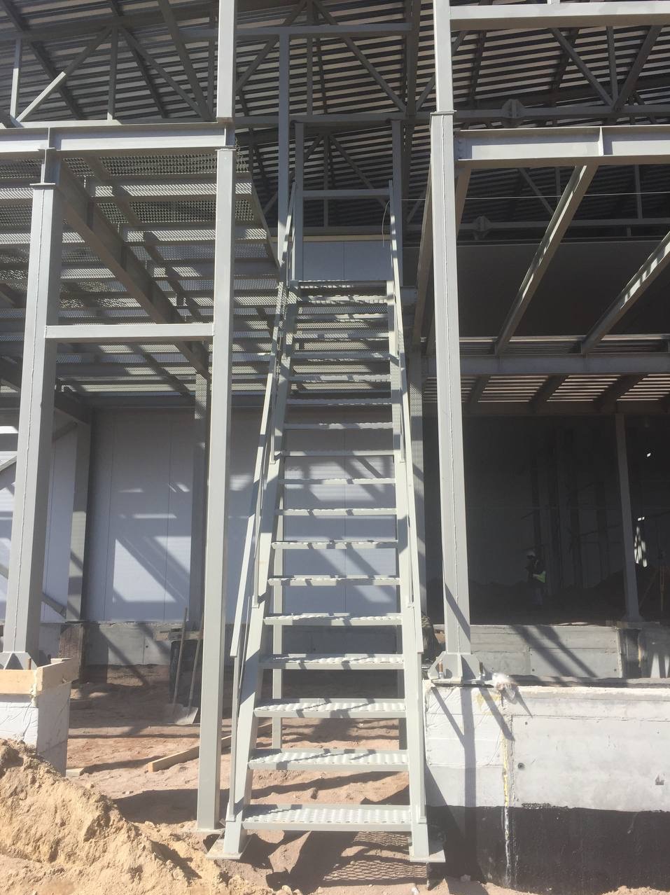 Szkielet hali przemysłowej w trakcie budowy z metalową konstrukcją, schodami i widocznym zarysem pracownika w środku.