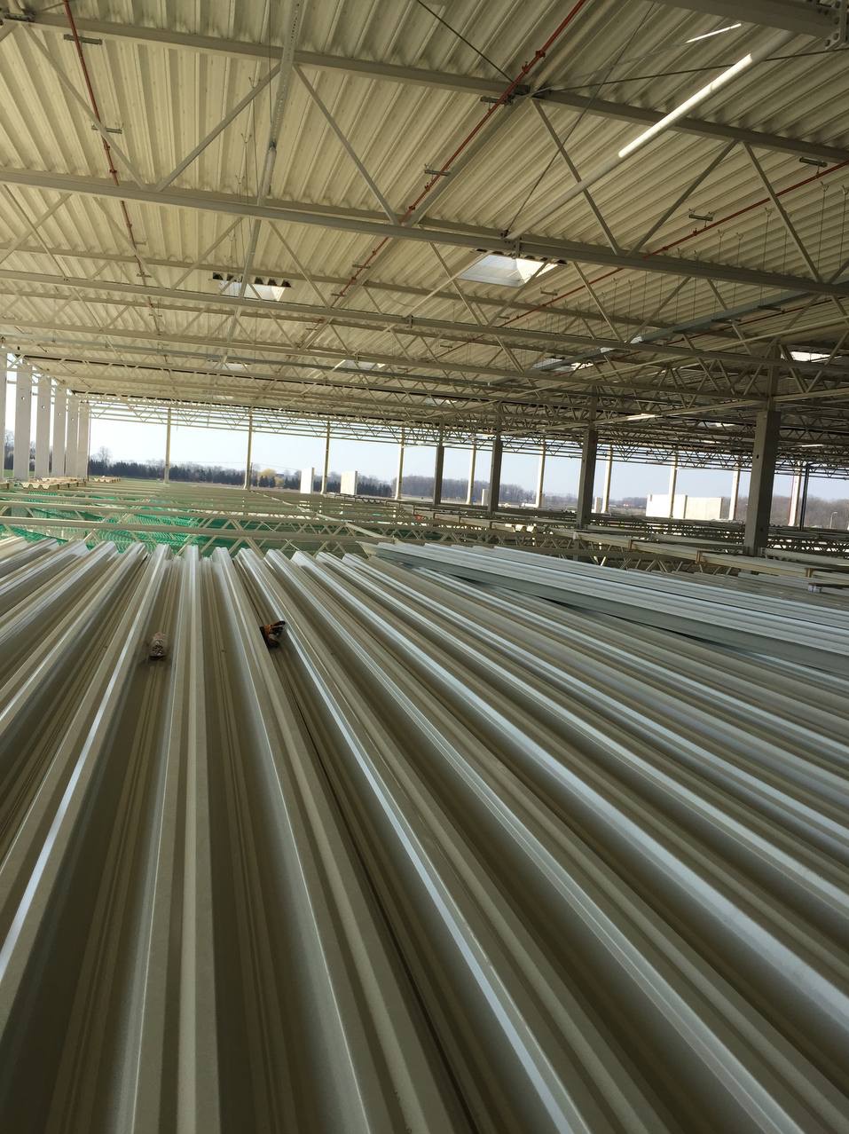 Wnętrze hali w trakcie budowy, widoczne ułożone płyty warstwowe na dachu, konstrukcja stalowa i oświetlenie.