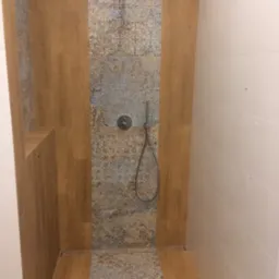 Wykończona kabina prysznicowa z drewnopodobnymi i wzorzystymi płytkami, odpływ liniowy, deszczownica. Nowoczesny design łazienki w neutralnych barwach.