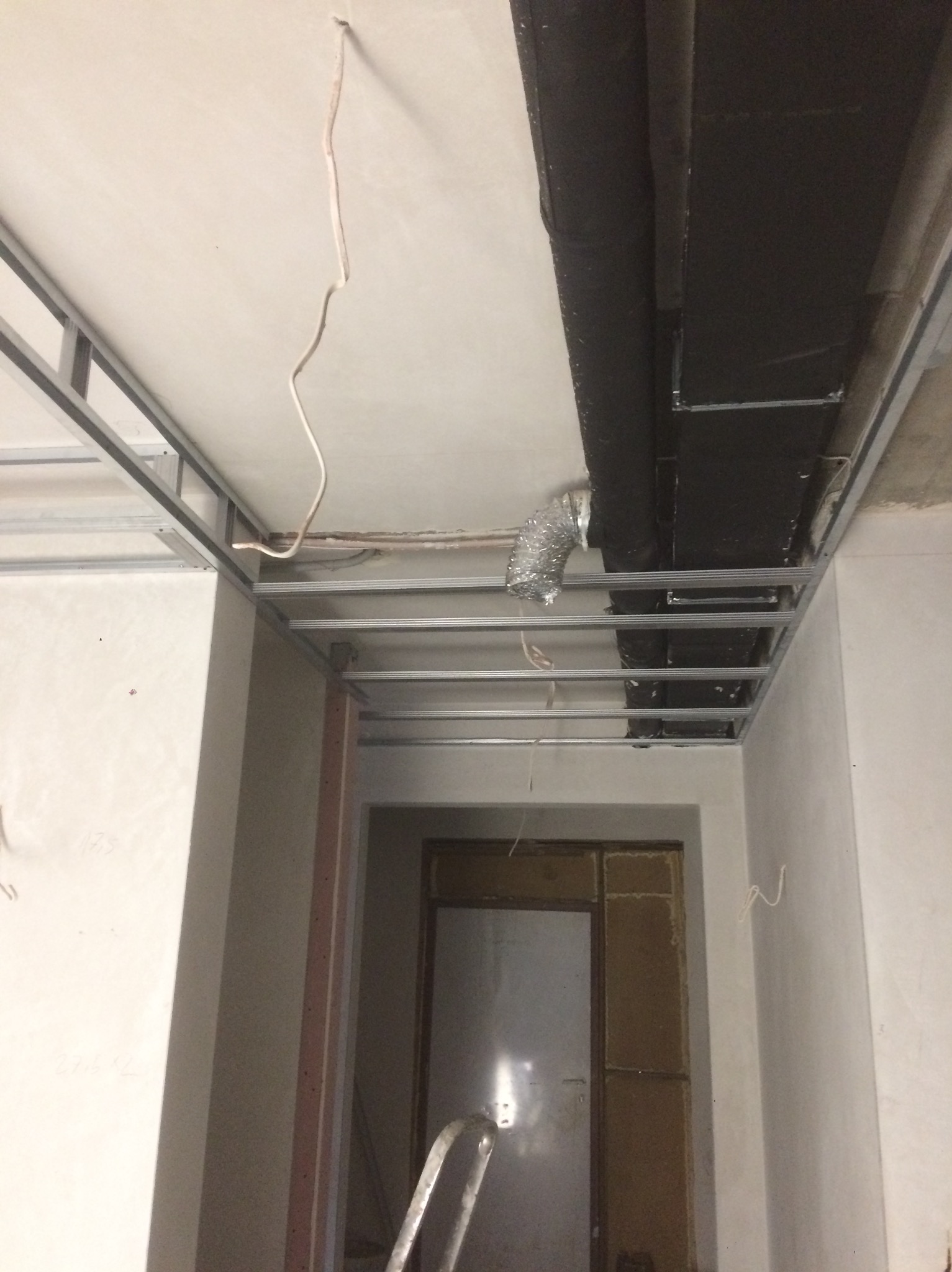 Metalowy stelaż sufitu podwieszanego z widocznymi przewodami wentylacyjnymi i elektrycznymi w trakcie montażu. Widoczny fragment drabiny.