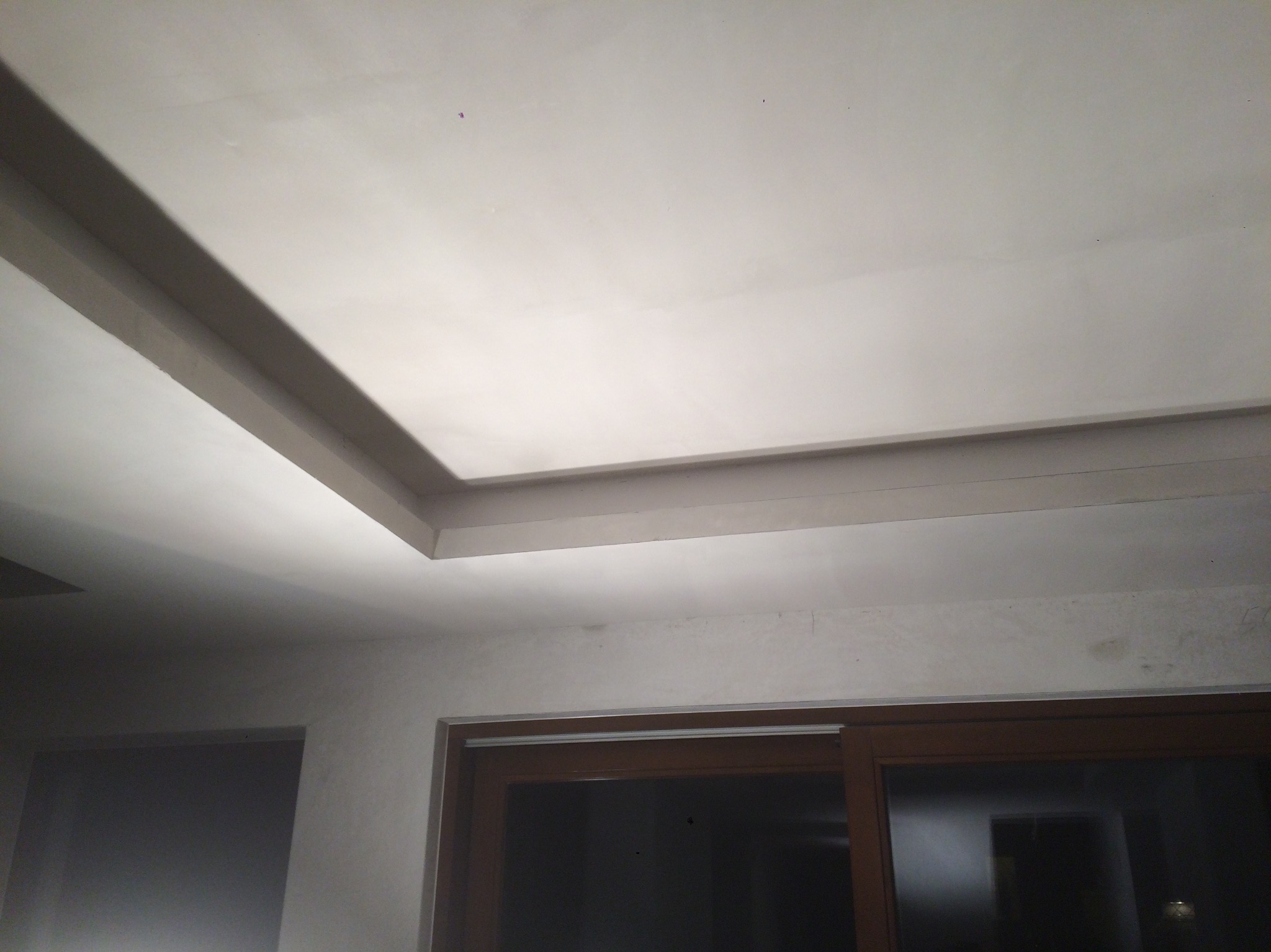 Gładki, biały sufit z dekoracyjnym podwieszanym elementem i oknem w tle. Świeżo wykończone ściany gotowe do malowania. Widok z dołu.