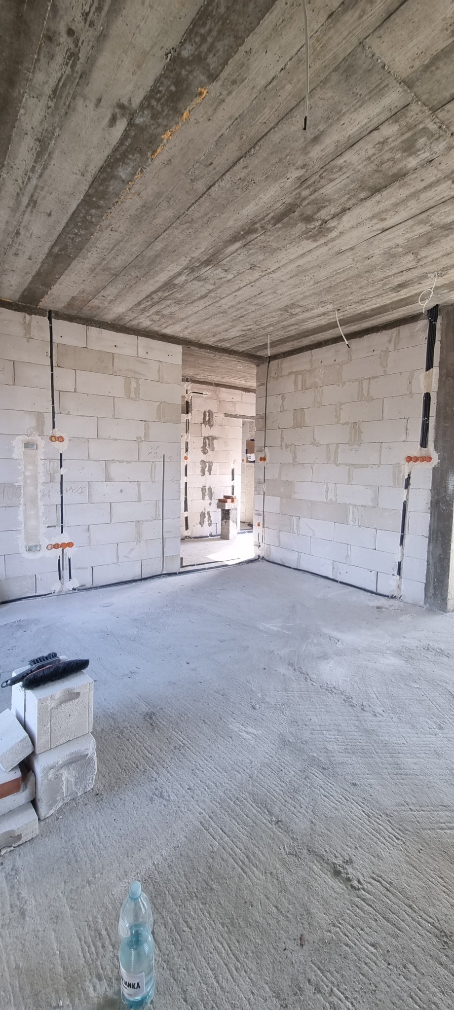 Surowy stan wnętrza z instalacją elektryczną w bruzdach ścian z betonu komórkowego. Widoczne kable i puszki. Na podłodze butelka wody i narzędzia.
