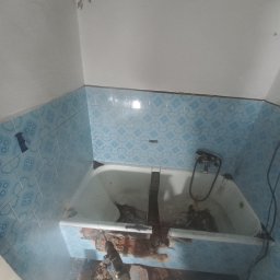 BARTŁOMIEJ GAŹDZIAK USŁUGI BUDOWLANE - Demontaż starej, niebieskiej glazury w łazience za pomocą młota udarowego, widoczna wanna i fragment instalacji wodnej.