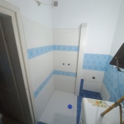 BARTŁOMIEJ GAŹDZIAK USŁUGI BUDOWLANE - Wykończona łazienka z biało-niebieskimi płytkami, kabiną prysznicową bez brodzika i widoczną pralką z żółtymi rurami.