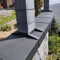 Czarno-szara elewacja ogrodzenia z kamienia łupanego i elementów betonowych, widok z bliska na konstrukcję.