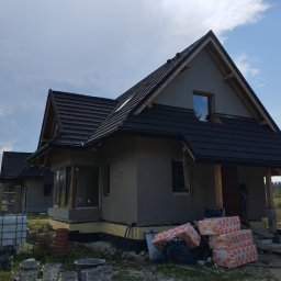 BARTŁOMIEJ GAŹDZIAK USŁUGI BUDOWLANE - Dom w Frydmanie w trakcie ocieplania elewacji, widoczne materiały izolacyjne i puste wiadra po farbie, częściowo otynkowana fasada i czarna dachówka.