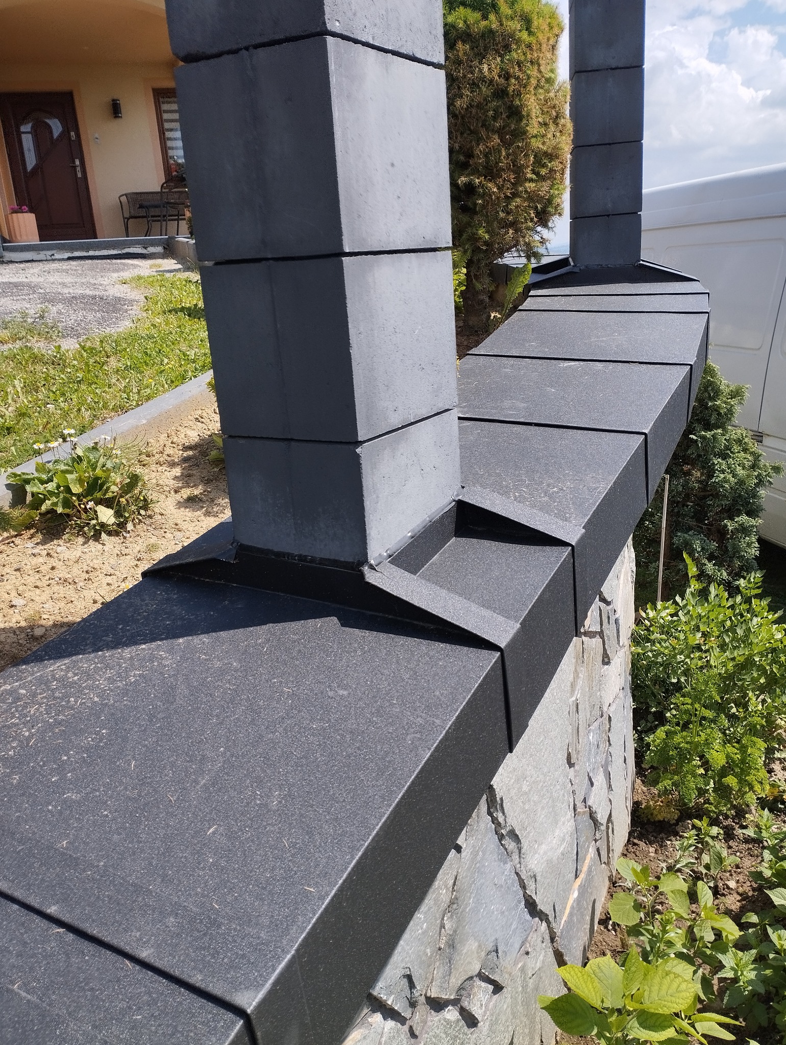 Czarno-szara elewacja ogrodzenia z kamienia łupanego i elementów betonowych, widok z bliska na konstrukcję.