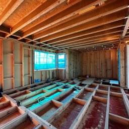 Royal Bud - Wnętrze domu w trakcie budowy: drewniana konstrukcja szkieletowa ścian, belek stropowych i podłogi. Okna zabezpieczone folią. Widoczne instalacje.