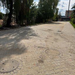 Royal Bud - Ułożona kostka brukowa na placu z drzewami w tle, widoczne studzienki kanalizacyjne i krawężnik. Świeżo wykonana nawierzchnia z kostki.