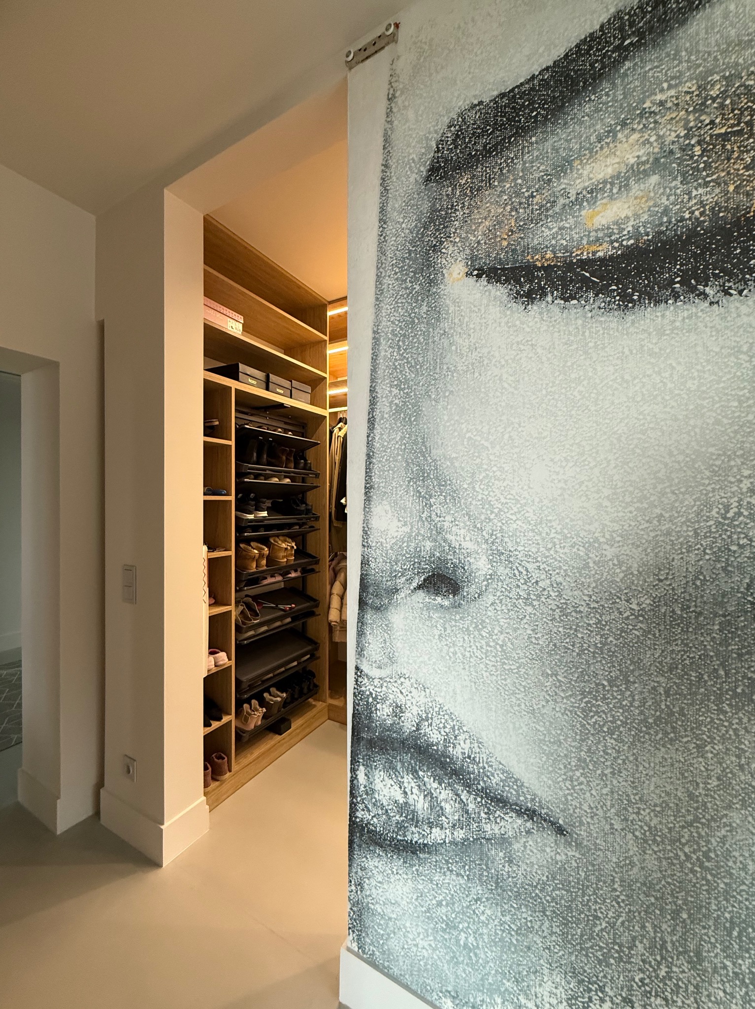 Nowoczesna garderoba z oświetleniem LED i przesuwnymi drzwiami z artystycznym malunkiem twarzy, widok z korytarza.