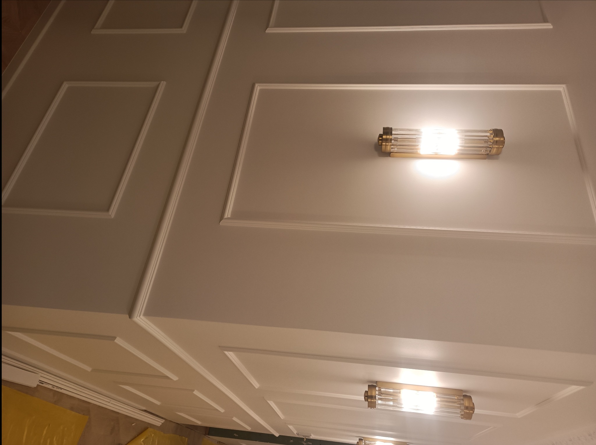 Ściana z dekoracyjnymi listwami i nowoczesnymi kinkietami z elementami w kolorze złota, widok z dołu.