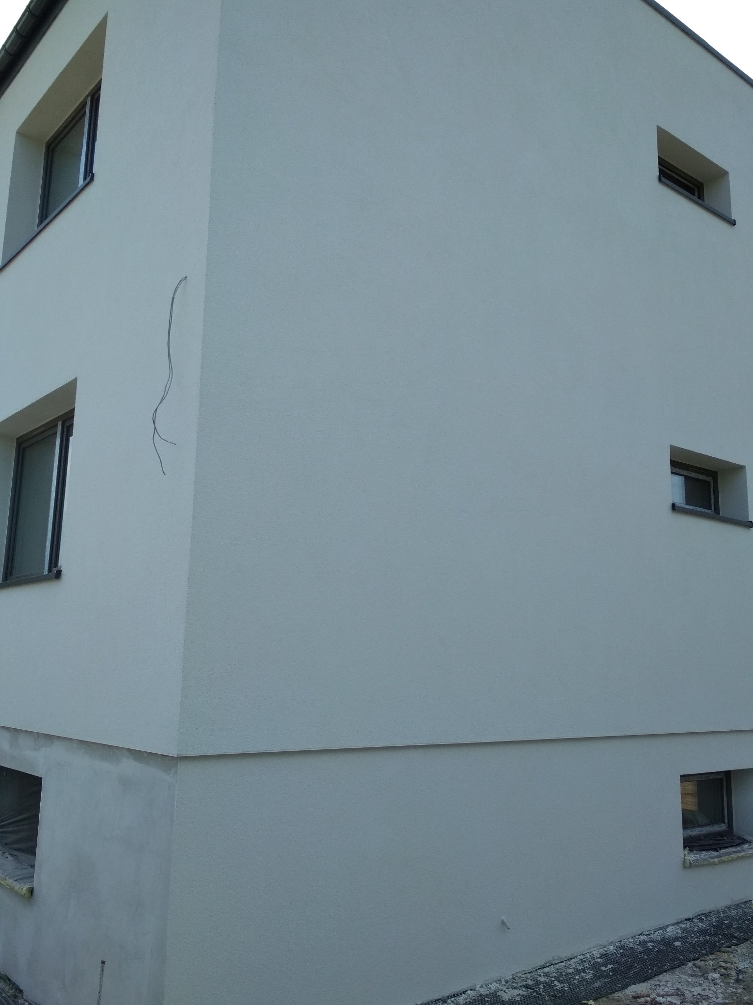 Fragment elewacji budynku po ociepleniu, z widocznymi oknami i wystającymi przewodami na rogu ściany.