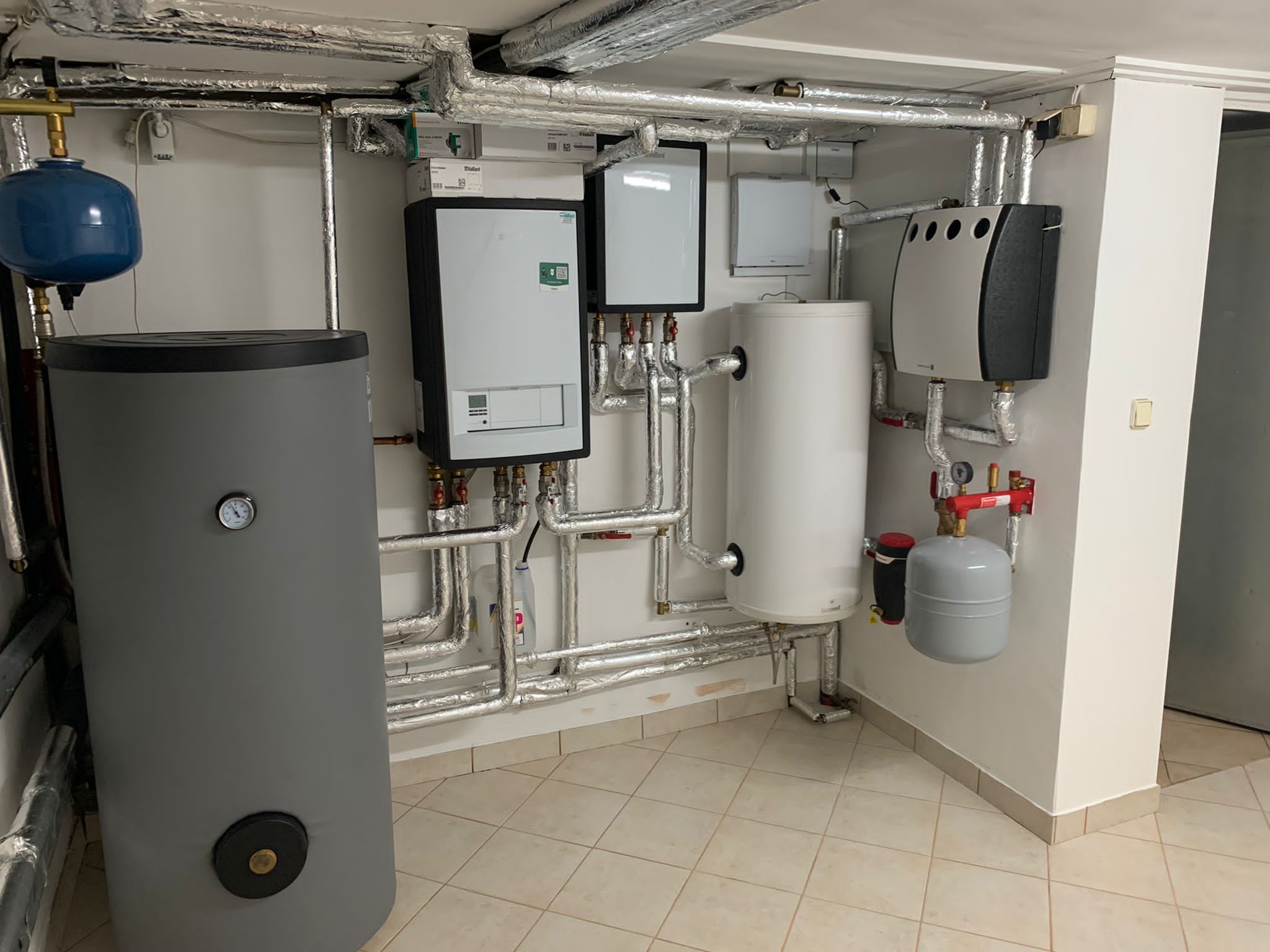 Kotłownia z zainstalowanymi urządzeniami: zbiornik buforowy, jednostka grzewcza, naczynia przeponowe i rury w izolacji termicznej.