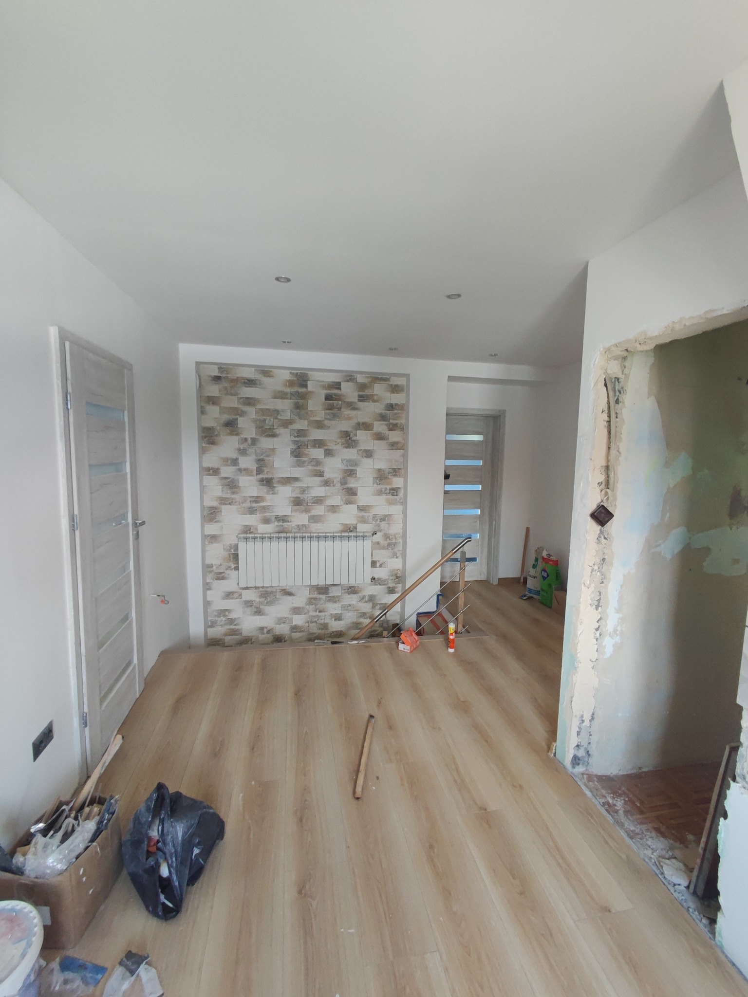 Wnętrze w trakcie remontu: ułożona podłoga z paneli, fragment ściany z dekoracyjną okładziną imitującą cegłę i grzejnikiem, widoczne narzędzia i materiały budowlane, surowe wykończenie otworu...