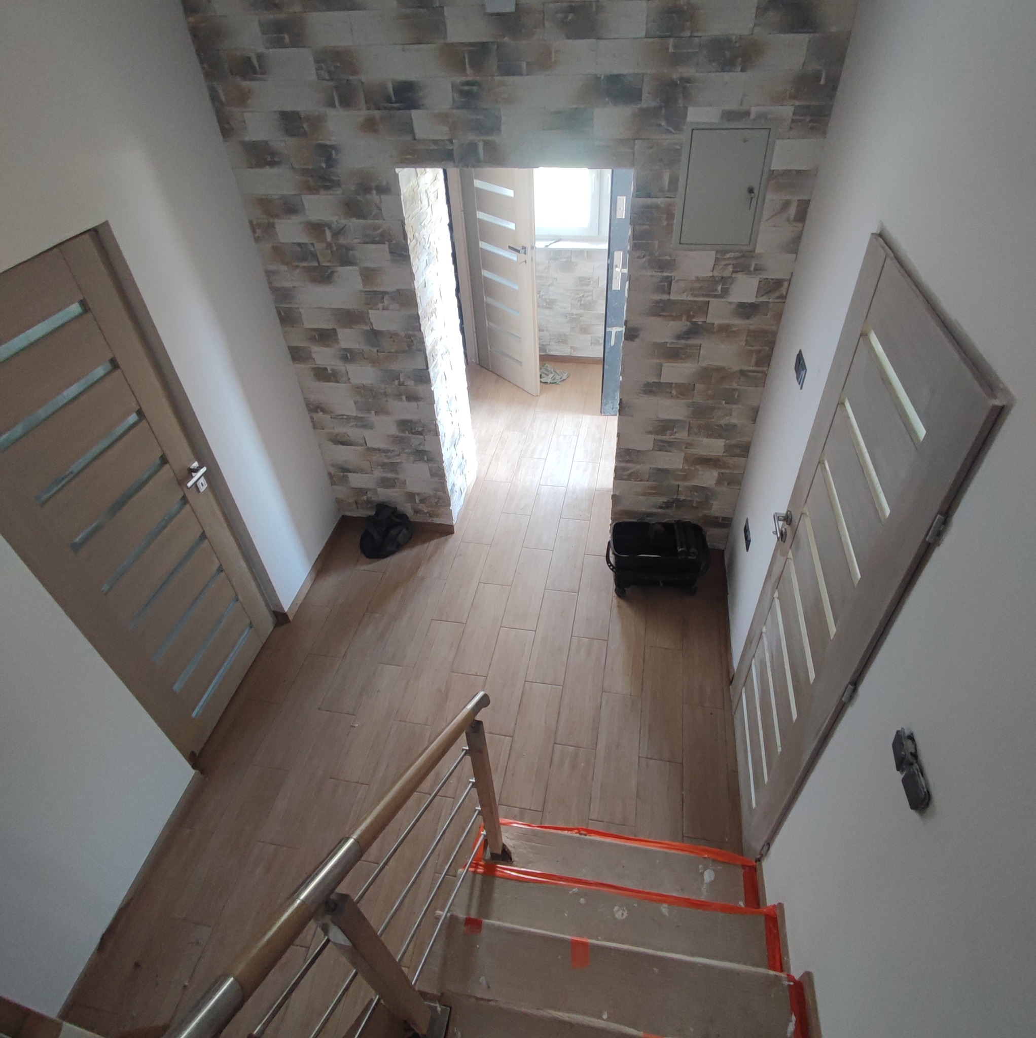 Widok z góry na korytarz w Radziszowie po remoncie: położona terakota imitująca drewno, ściany wyłożone dekoracyjną cegłą, widoczne dwie drewniane drzwi z przeszkleniami oraz schody...