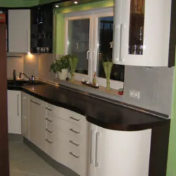 Nowoczesna kuchnia z białymi szafkami z zaokrąglonymi narożnikami, ciemnym blatem i szarymi płytkami nad zlewem, z oknem z roślinami i dekoracjami.