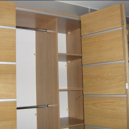 M.Serwis Polonis G. - Otwarta szafa wnękowa z przesuwnymi drzwiami z jasnego drewna z poziomymi, metalowymi wstawkami, widoczne półki i drążek na ubrania, wnętrze szafy w kolorze jasnego drewna i bieli.