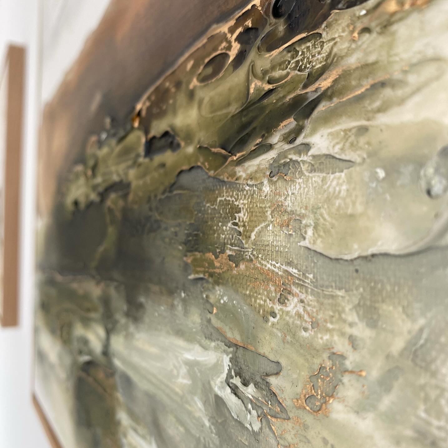 Abstrakcyjna faktura farby w odcieniach brązu, zieleni i bieli z metalicznymi złotymi akcentami, widoczna z bliskiej perspektywy pod kątem.