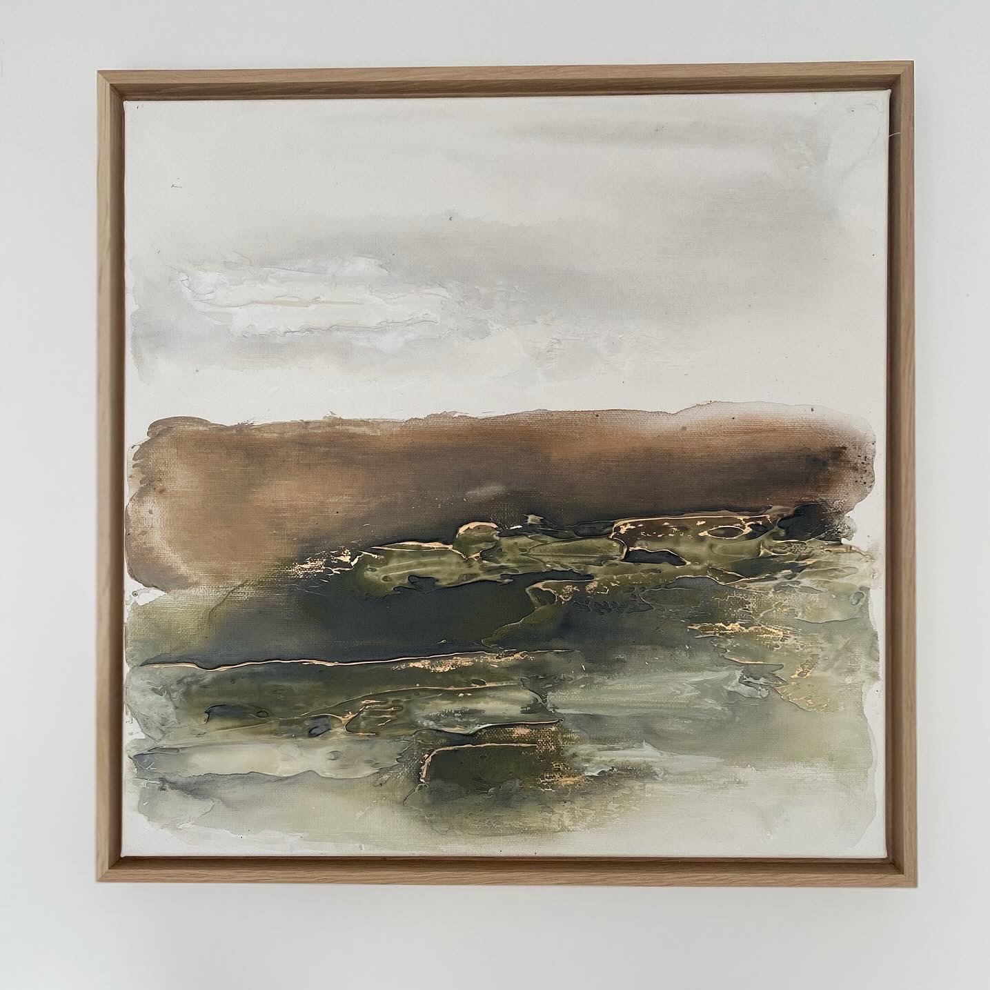 Abstrakcyjny obraz w drewnianej ramie, z przewagą brązów, zieleni i szarości, z akcentami złota, przypominający pejzaż z ziemią, wodą i niebem.