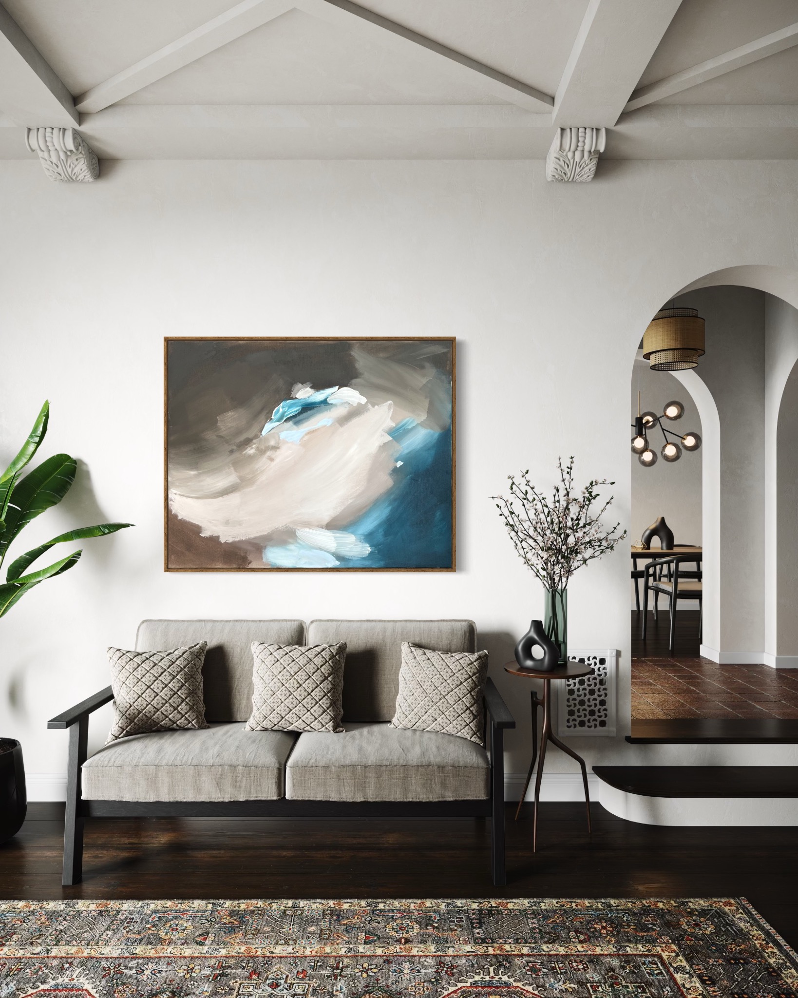 Abstrakcyjny obraz w brązowo-niebieskiej tonacji nad szarą sofą z poduszkami w salonie z ciemną podłogą i łukowatym przejściem do jadalni.
