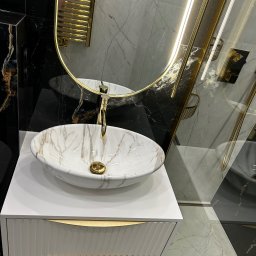 RH-BUD - Elegancka umywalka nablatowa z marmurowym wzorem, złota armatura, biała szafka z frezowanymi frontami i złote detale, lustro z podświetleniem LED, czarno-białe marmurowe płytki na ścianie i podłodze.