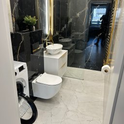 RH-BUD - Elegancka łazienka z czarnymi marmurowymi ścianami, złotymi akcentami i nowoczesną armaturą. Widoczna pralka z otwartymi drzwiami i marmurowa podłoga.