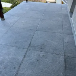 Wykończony balkon z szarymi, kwadratowymi płytkami. Widok z góry, ukazujący równo ułożoną podłogę i elementy konstrukcyjne balkonu. Minimalistyczny design.