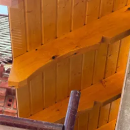 Jasna, drewniana więźba dachowa z widocznymi belkami i deskowaniem, sfotografowana z dołu pod kątem. Widoczne rusztowanie i fragment muru.