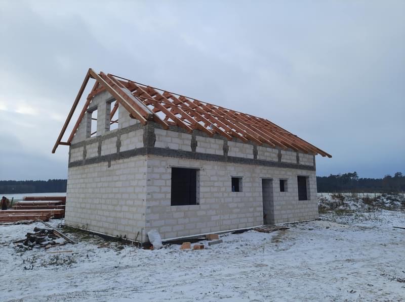 Surowy stan domu z białych bloczków w zimowym krajobrazie, widoczna konstrukcja więźby dachowej, przygotowana do dalszych prac.