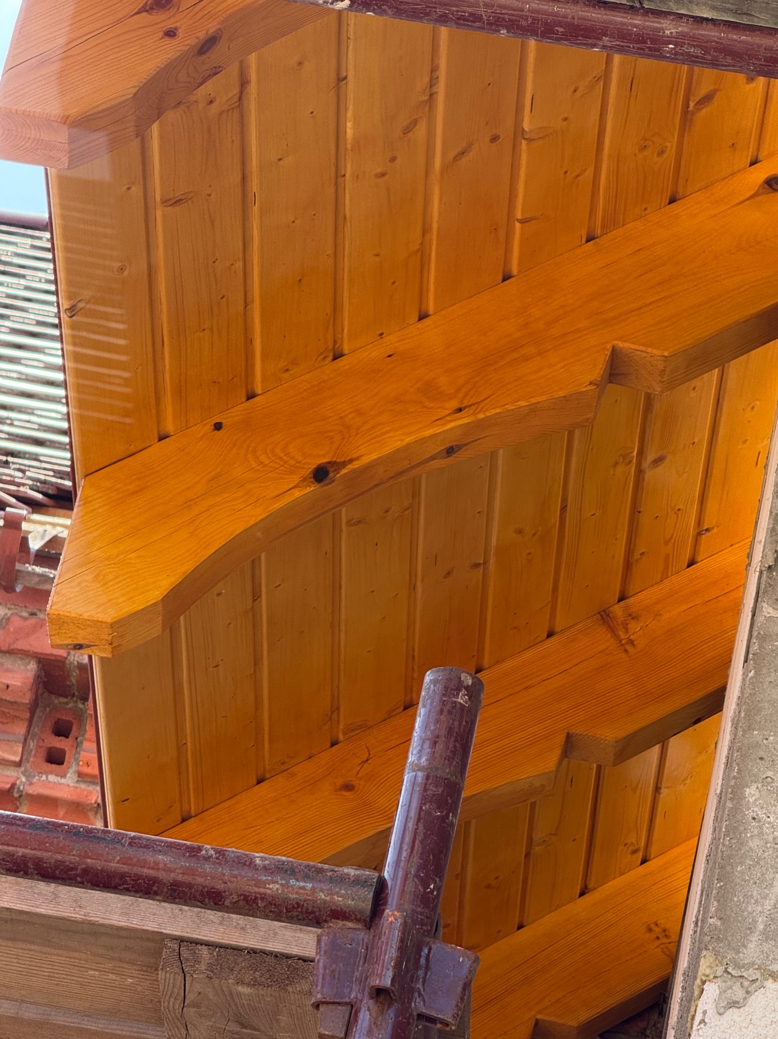 Jasna, drewniana więźba dachowa z widocznymi belkami i deskowaniem, sfotografowana z dołu pod kątem. Widoczne rusztowanie i fragment muru.