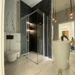 Vitalii Herasymenko - Nowoczesna łazienka z kabiną prysznicową typu walk-in, umywalką wolnostojącą i podwieszaną toaletą, wykończona płytkami imitującymi marmur w kolorze białym i czarnym ze złotymi żyłami.