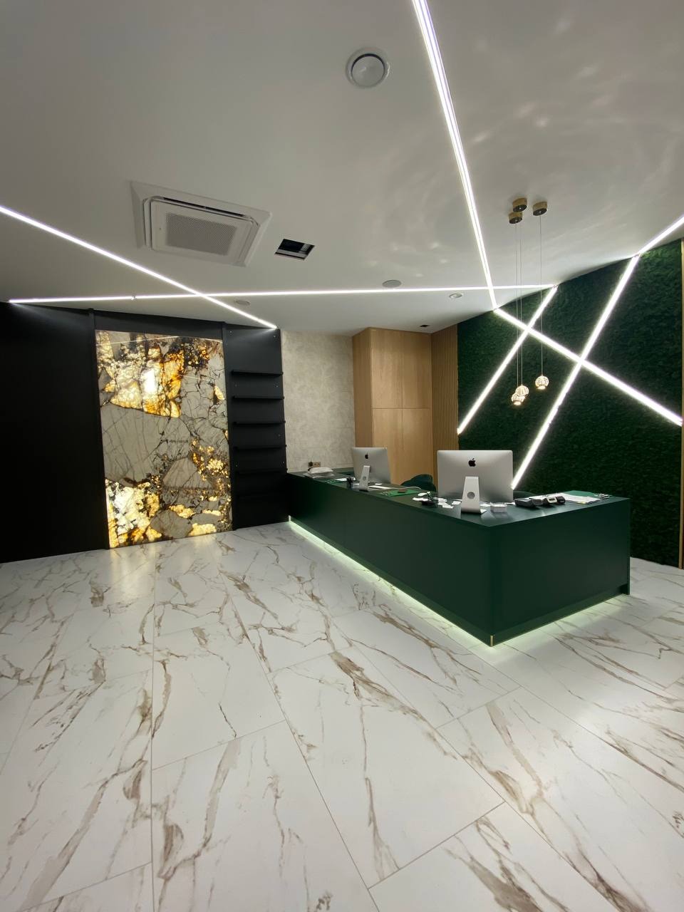 Nowoczesne wnętrze recepcji z podświetlaną ladą w kolorze butelkowej zieleni, marmurową posadzką, dekoracyjną ścianą z mchu i podświetleniem LED na suficie.