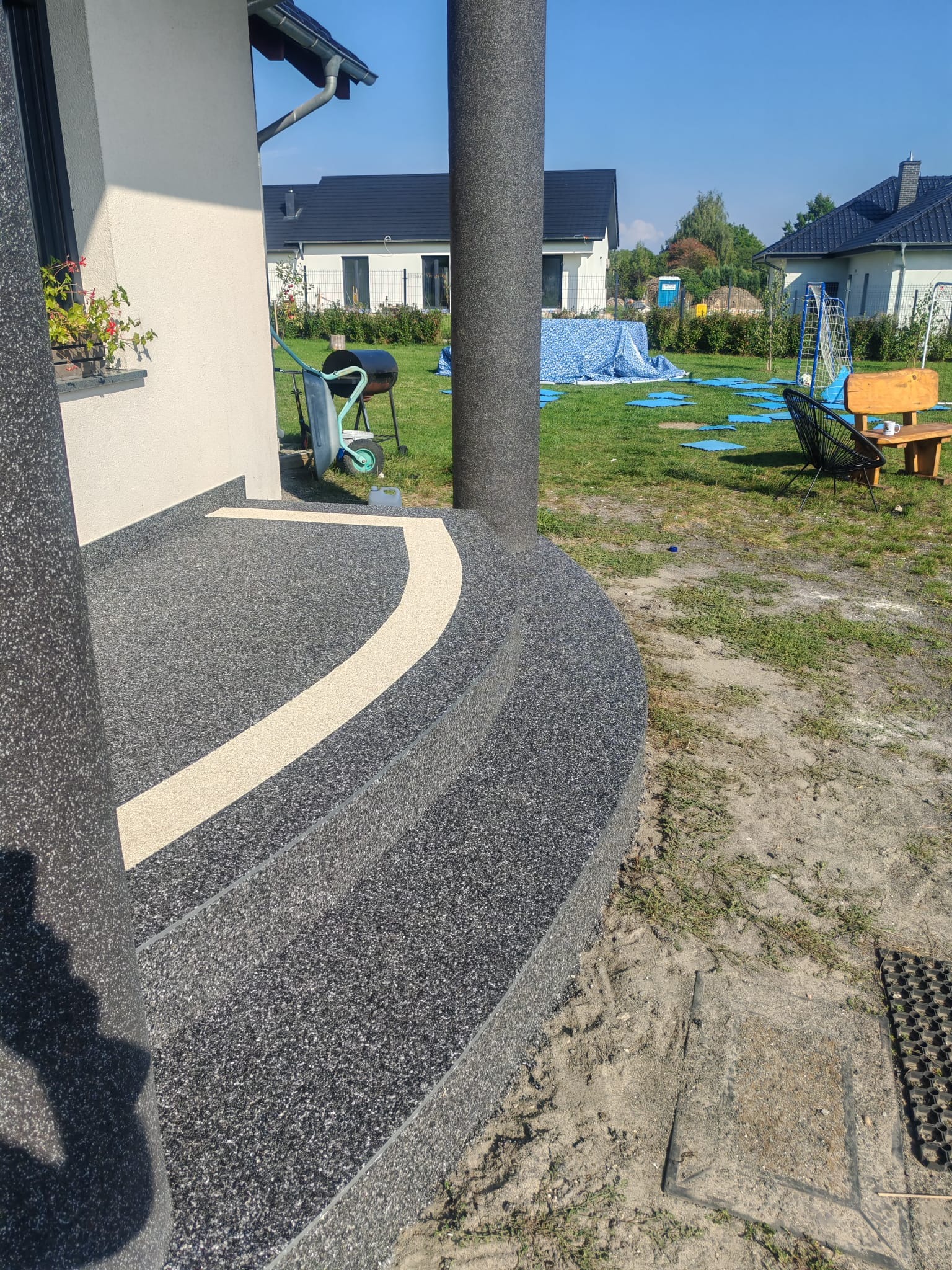 Granitowe schody wejściowe z żywicy epoksydowej, z jasnym akcentem, prowadzące do domu z ogrodem. Widoczne kolumny i elementy architektury.