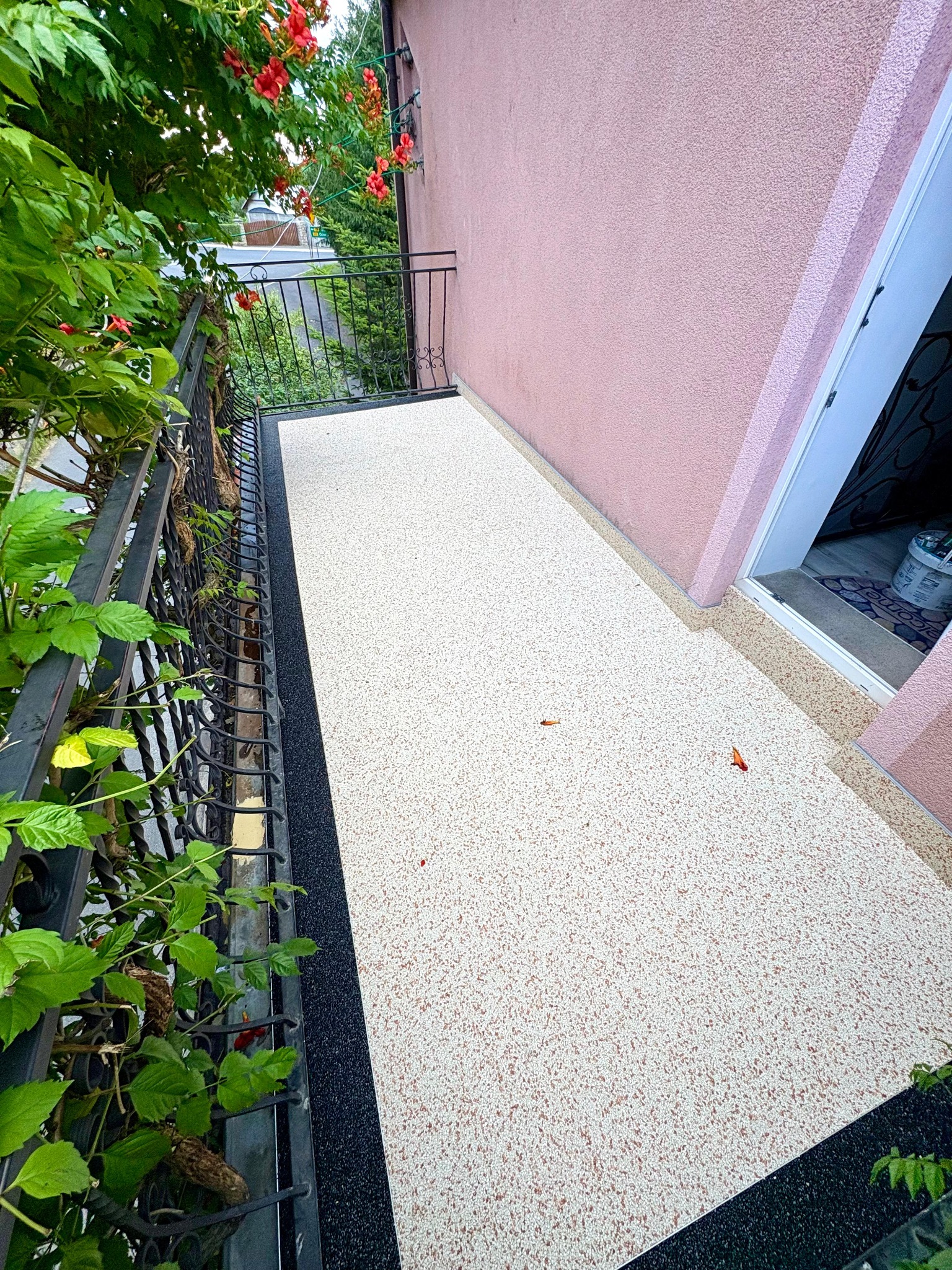 Jasna posadzka żywiczna na balkonie z czarną obwódką, widok z góry, kwiaty zwisają z balustrady. Wykończenie balkonu w nowoczesnym stylu.