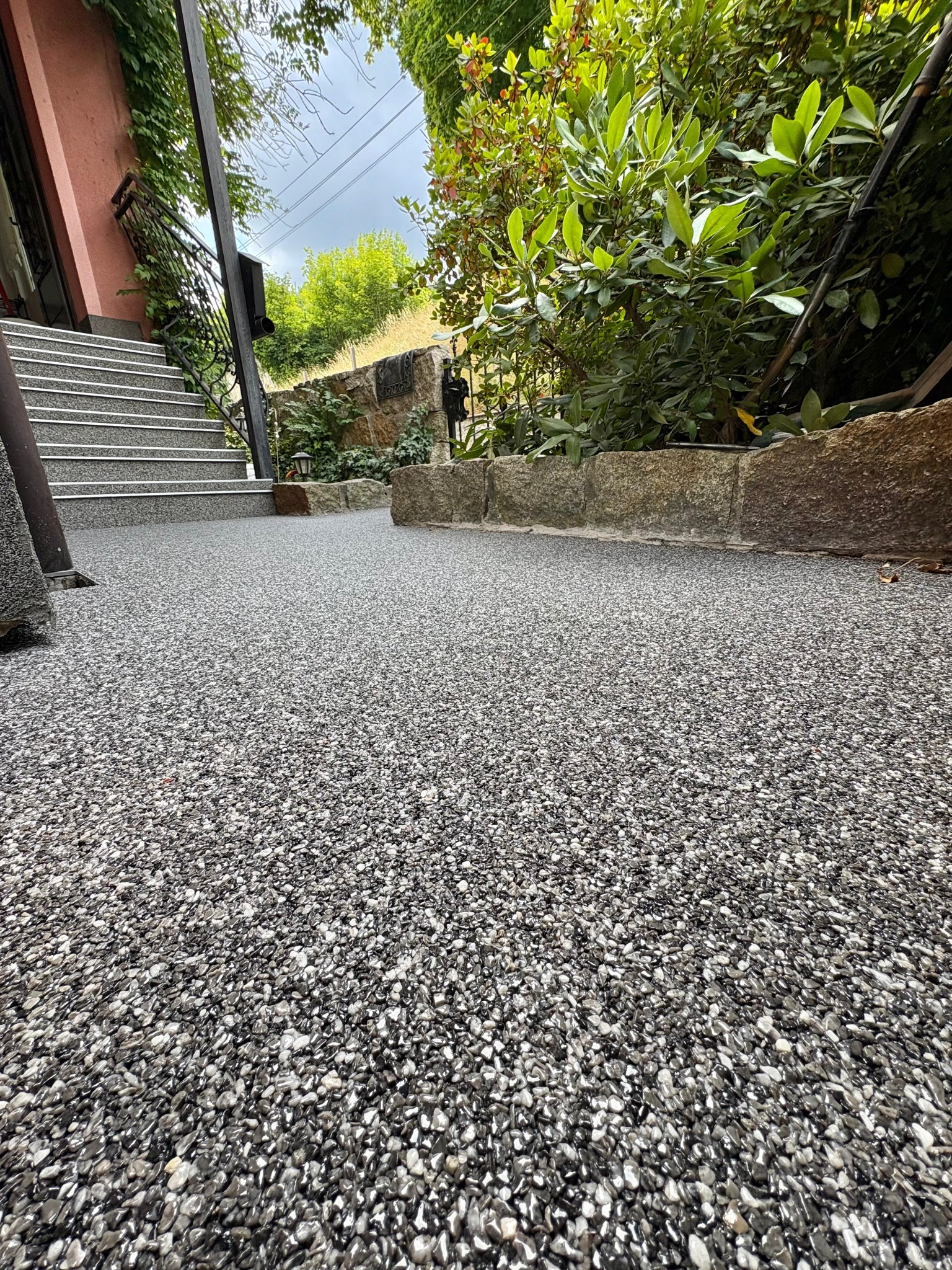 Szara posadzka żywiczna z drobnymi kamyczkami prowadząca do schodów i ogrodu, z niskiej perspektywy, ukazująca detale tekstury i otoczenie.