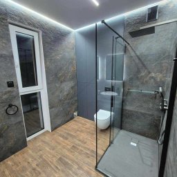 Magkambud - Nowoczesna łazienka z szarymi płytkami imitującymi kamień, drewnopodobną podłogą, kabiną prysznicową typu walk-in z czarnymi profilami i oświetleniem LED w suficie.