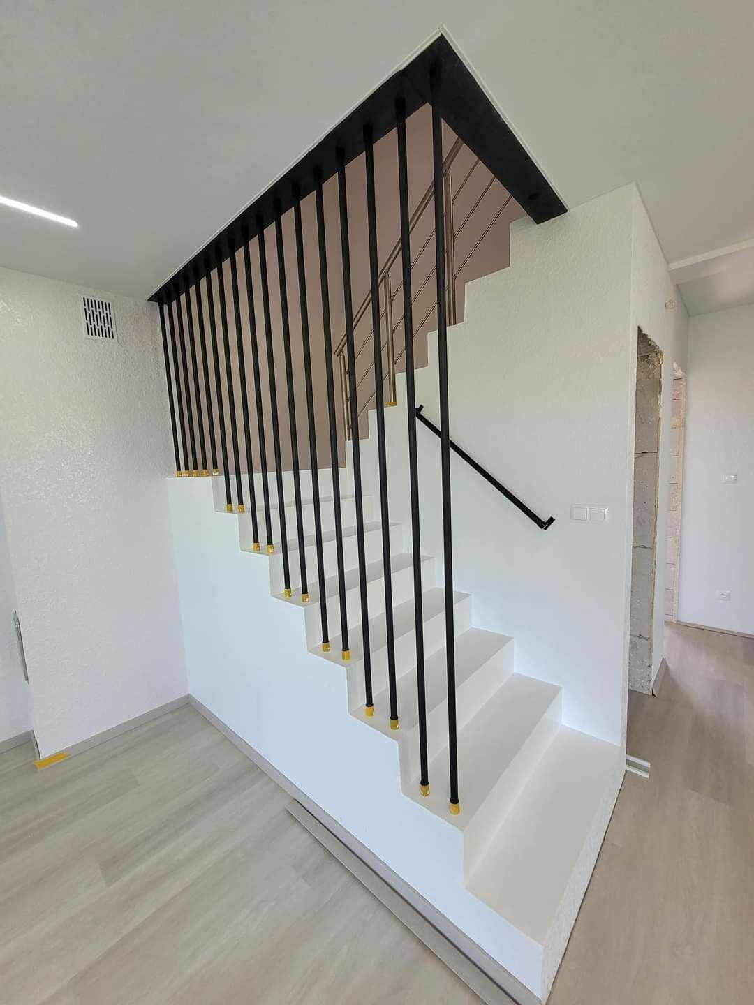 Nowoczesne, białe schody z czarną balustradą i złotymi detalami, wykończone wnętrze z jasną podłogą.