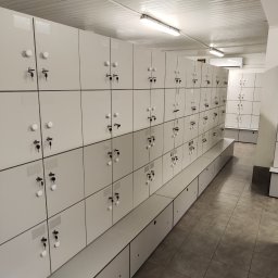 Kamil Wąsik - Rząd białych szafek zamykanych na klucz w szatni, widoczne klucze w zamkach, na podłodze płytki imitujące kamień, na jednej z szafek kartka z informacją o wymianie szafek.