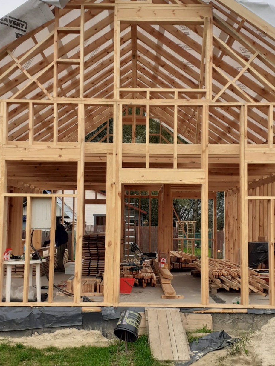 Surowa drewniana konstrukcja domu w trakcie budowy, widoczne elementy szkieletu, narzędzia i materiały budowlane wewnątrz.