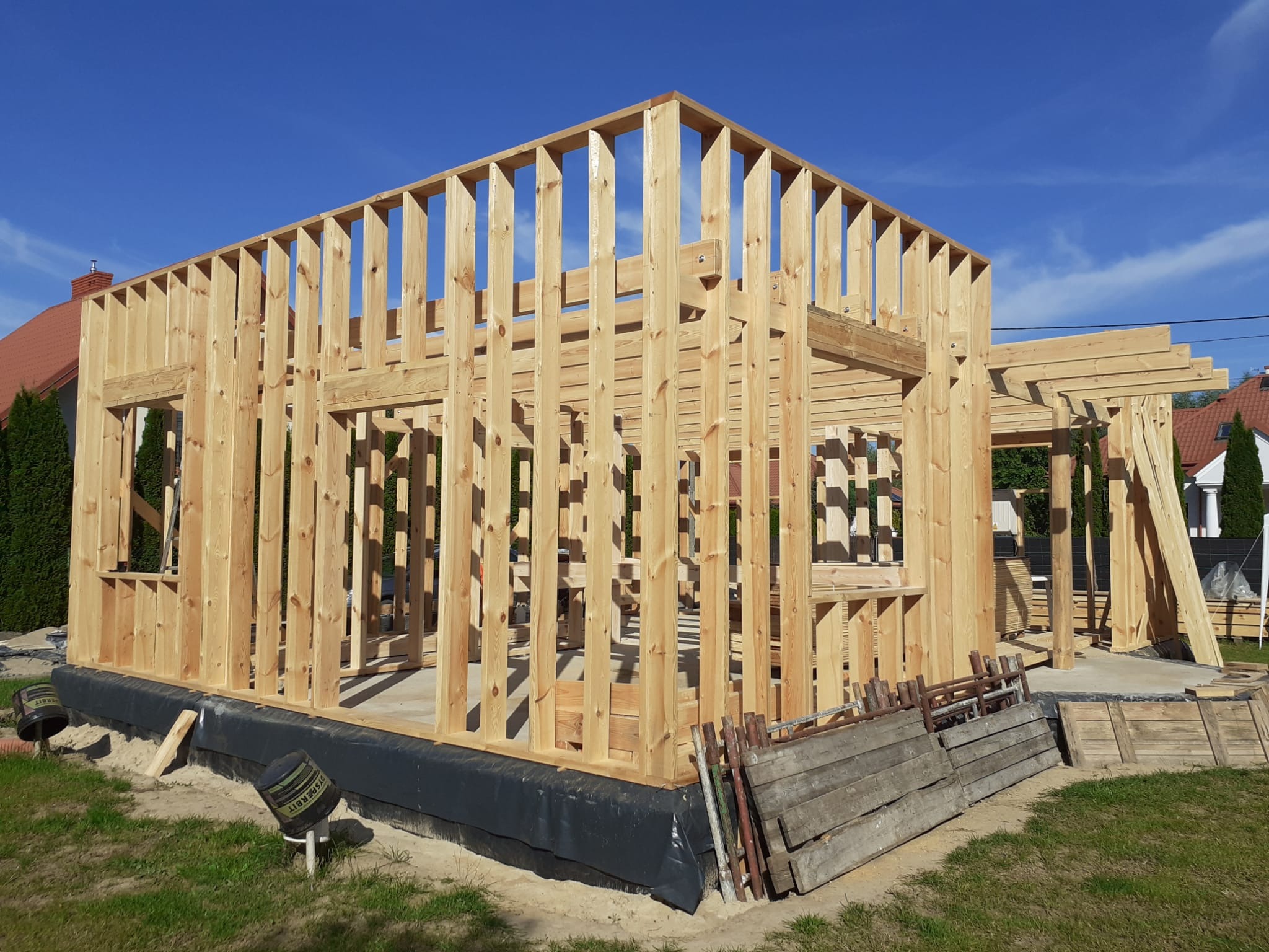 Konstrukcja nośna z drewna, wznoszona na fundamencie z izolacją przeciwwilgociową, widok w słoneczny dzień.